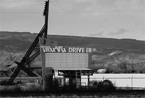 A photo of the drive in in black and white with hills behind and prominent sign in the center. 