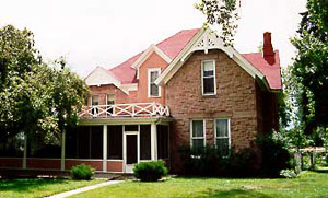 A picture of the house with a mix of gable and hip roofs with long porch on the left and balcony above.