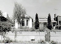 A black and white photo of the house with gabled window and cross section. Beneath the gable is a bay window and trees in the foreground.