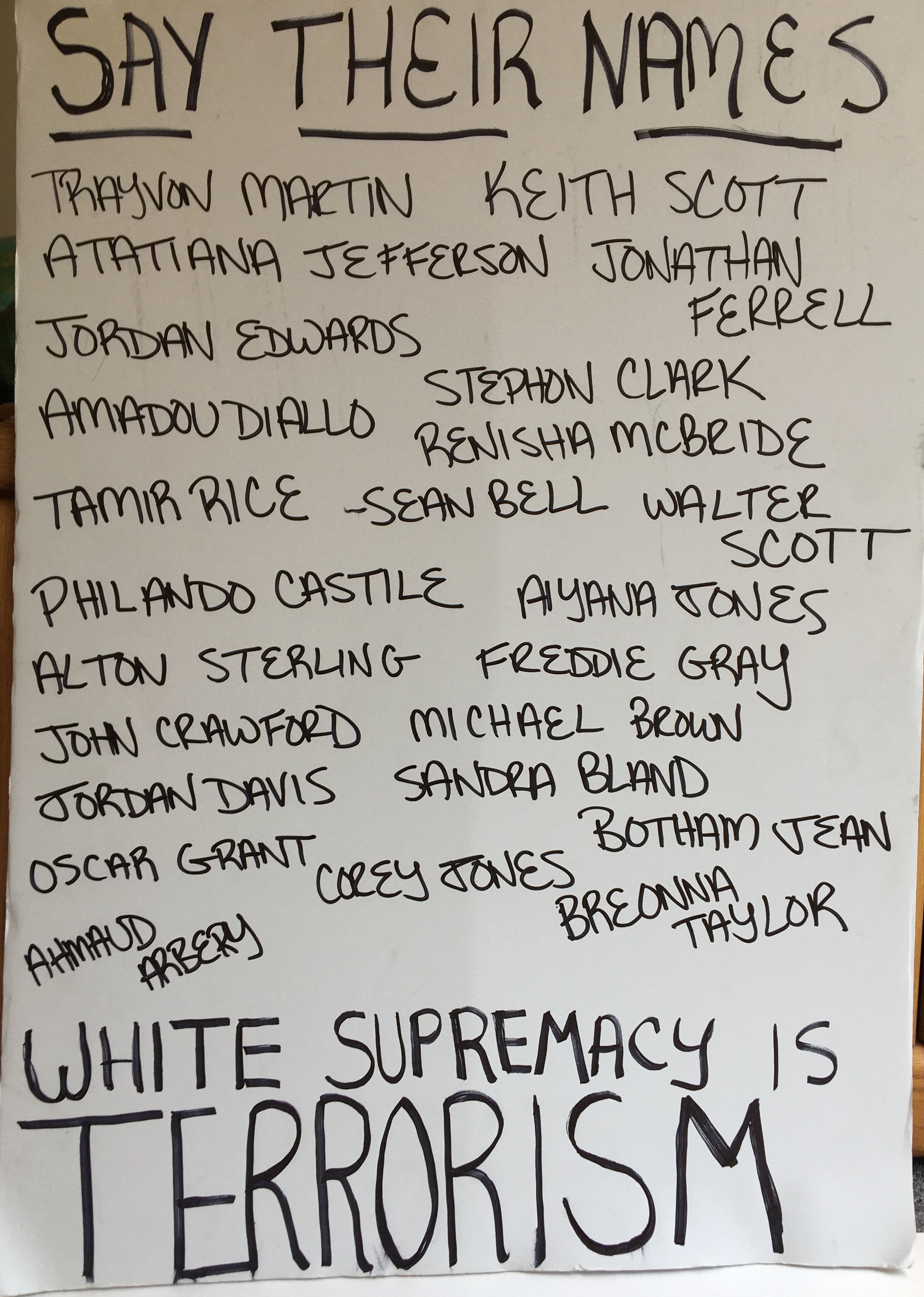Photo of a protest sign from a Black Lives Matter protest. Made of white paper and written on in black pen it says, from top to bottom: "Say their names" and lists the names of 24 people including Trayvon Martin, George Floyd, Breonna Taylor, Freddie Gray, Tamir Rice, and others. At the bottom, the sign says, "White supremacy is TERRORISM."