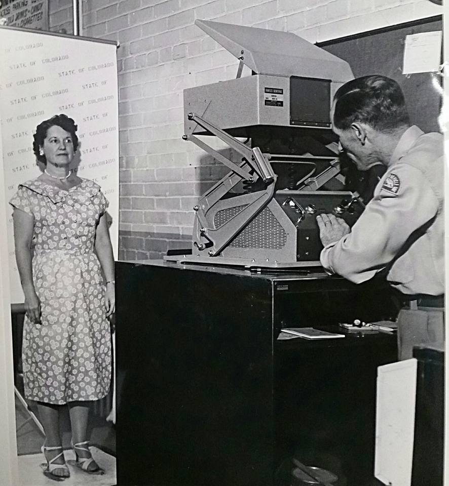 A woman poses in front of an antique camera.