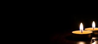 Two tea light candles are lit with a dark background