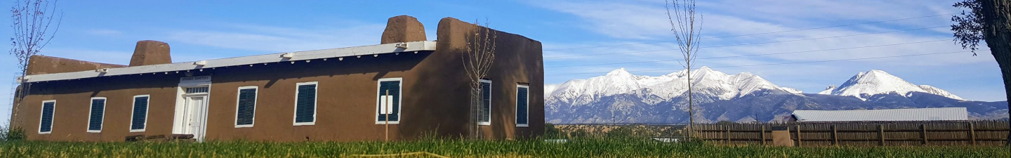Exterior of Fort Garland with snow-capped mountains behind an adobe building.