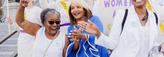 A large group of women gathered on the steps of the Capitol with protest signs and smiling.