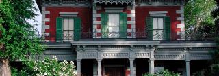 Exterior view of Bloom House, a four-story historical house, a stone stairway with railing leads to front entrance, intricate detailing on facade with green window shutters and bright red and white siding. 