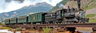A color photo of steam locomotive Engine 315, after restoration. The engine is under steam near Durango and hauling coal wagons. Mountains are visible behind.