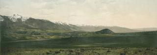 Colorized photograph of green prairie with snow-capped mountains in the background.