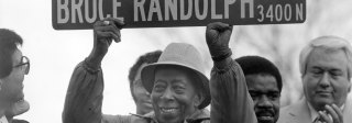 Bruce Randolph holding up a street sign which reads: "Bruce Randolph, Ave."