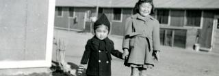 Two children, dressed for cold weather, pose before a barracks at the Amache incarceration camp.