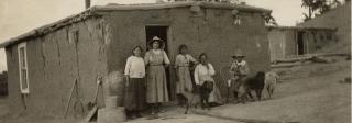 The Cisneros family posing for a family protrait in front of their adobe house.