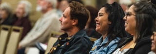 A diverse group of adults sit and smile while listening to a lecture at the History Colorado Center.