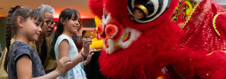 2 young girls greet a lion dancer with their grandmother.