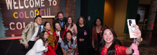 A group of people take a selfie at an event in the History Colorado Center atrium in front of the Welcome to Colorful Colorado sign.