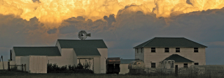 Huge rolling clouds descend on a white, historic Colorado ranch with a dark green roof.