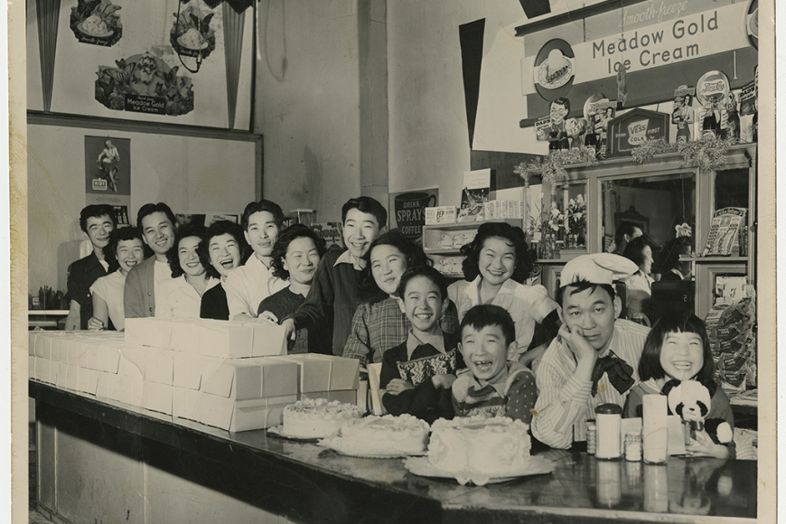 A large group of people behind an ice cream shop counter smiling.