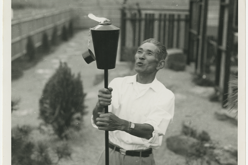 A man holding a lit tiki torch in a fenced in yard.