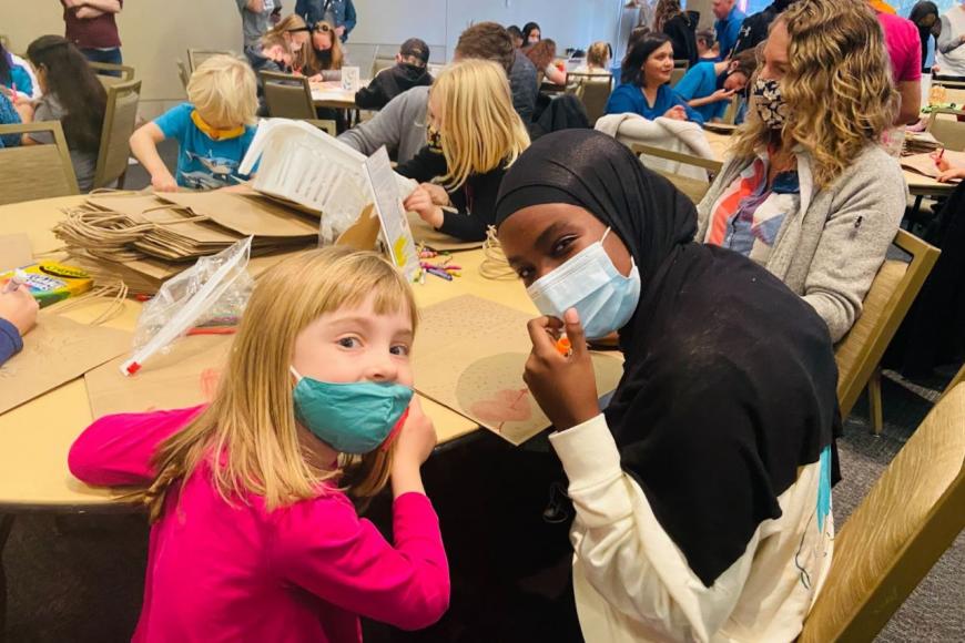 A Kramerica student volunteers with Family Day participants to make decorative bags for goods to be distributed to people in need. 