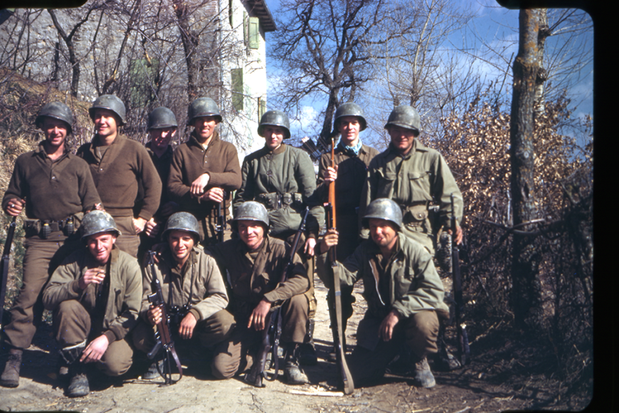 A group of 11 soldiers posing at camp hale and smiling. They have guns, bows and arrows, as well as grenades.