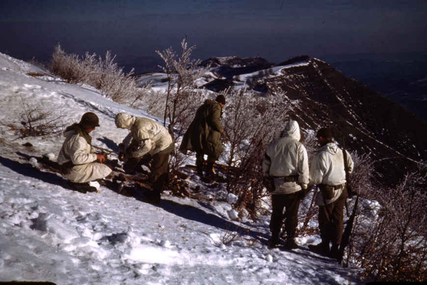 A group of soldiers standing on the side of a snowy winter mountain slope.