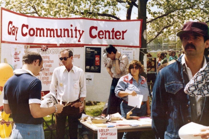 A group of people gathered outdoors in front of an informational banner and table.