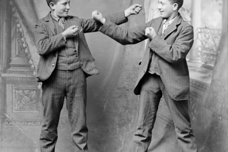 2 boys pose theatrically with their fists up in a studio portrait with drapes behind them.