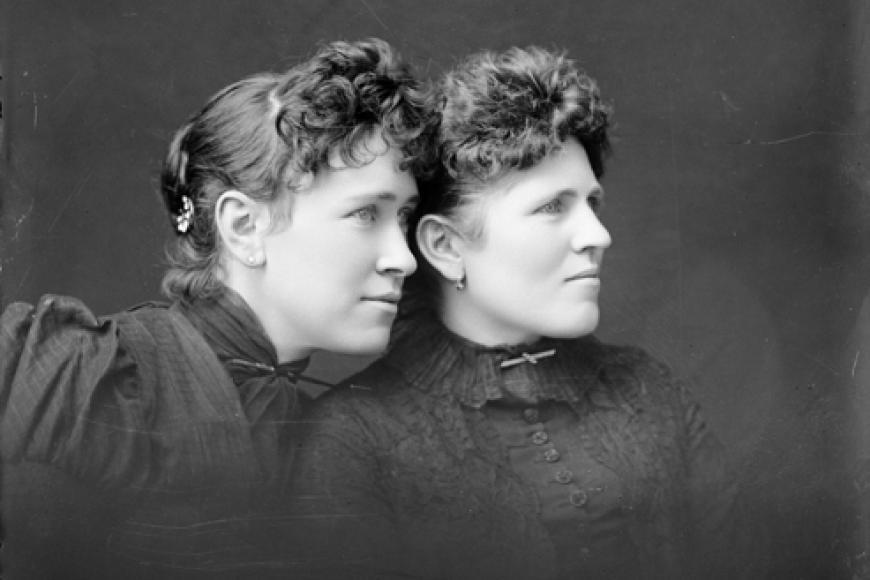 Profile photo of 2 caucasian women in victorian dress. They stare into the distance with the older woman behind the young. 