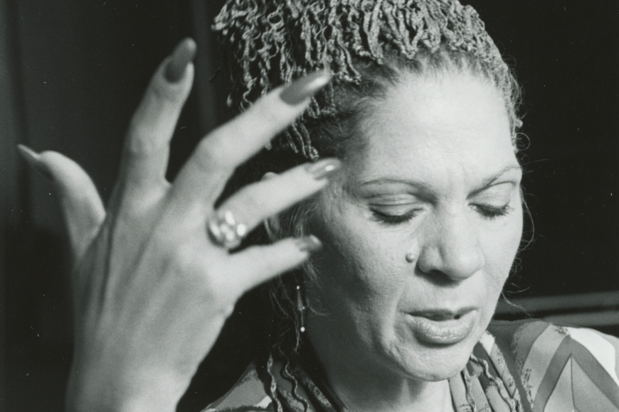 The photograph is a portrait, showing Robinson mid dance with her right hand upright in the air. She is wearing a colorful robe or shirt, and looking down as she moves.