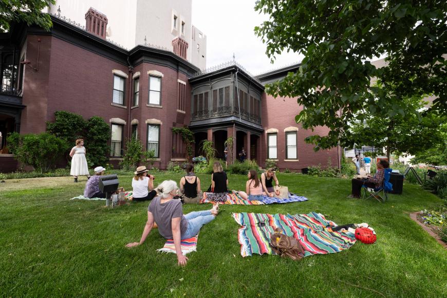 Exterior of center for Colorado Women's History and lawn, a group of visitors sit on the grass looking at a standing presenter.