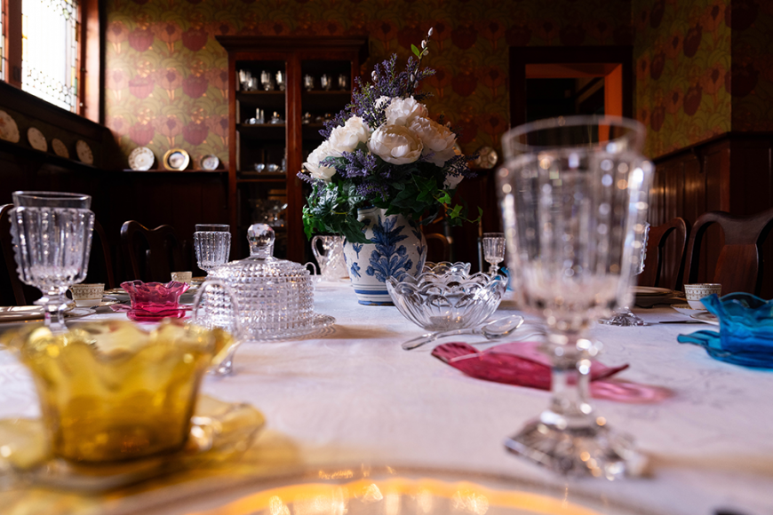 Close up of the dining table and glass place settings. There is a pink bouquet in a vase at the center of the table.
