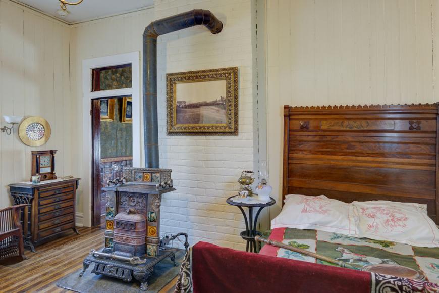 A bedroom furnished with a bed and a colorful, decorative wood burning stove.