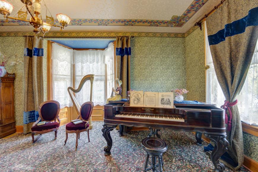 A Victorian furnished room with a grand piano, two velvet chairs and a harp.