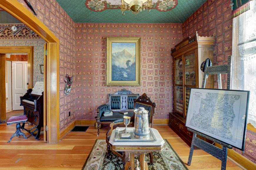 A colorfully wallpapered furnished room featuring a glass dish cabinet.