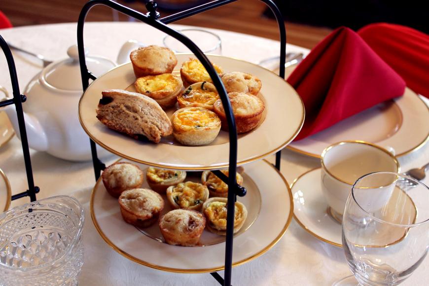 Overhead shot of double decker tea plate filled with scones, quiches, cookies, and scones on a white clothed table.