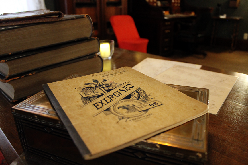 Stack of books on a wooden table. At the top, an old pamphlet reads 'Exercises.'