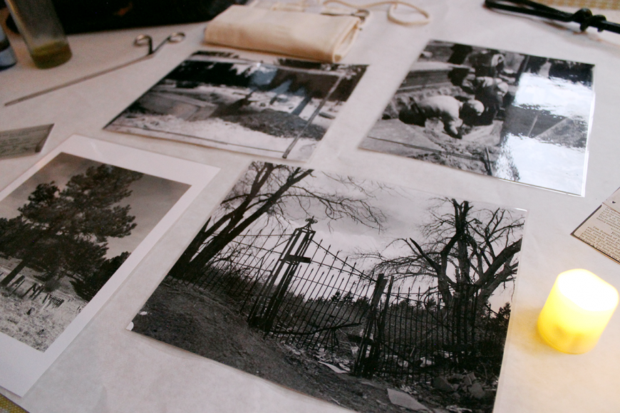Table covered in a myriad of black and white photographs showing Colorado graveyards. There is a candle beside the photos.