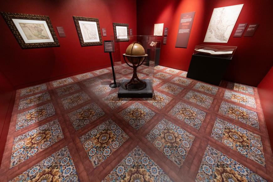 Interior of a red room lined with old maps. An antique globe is at the center.