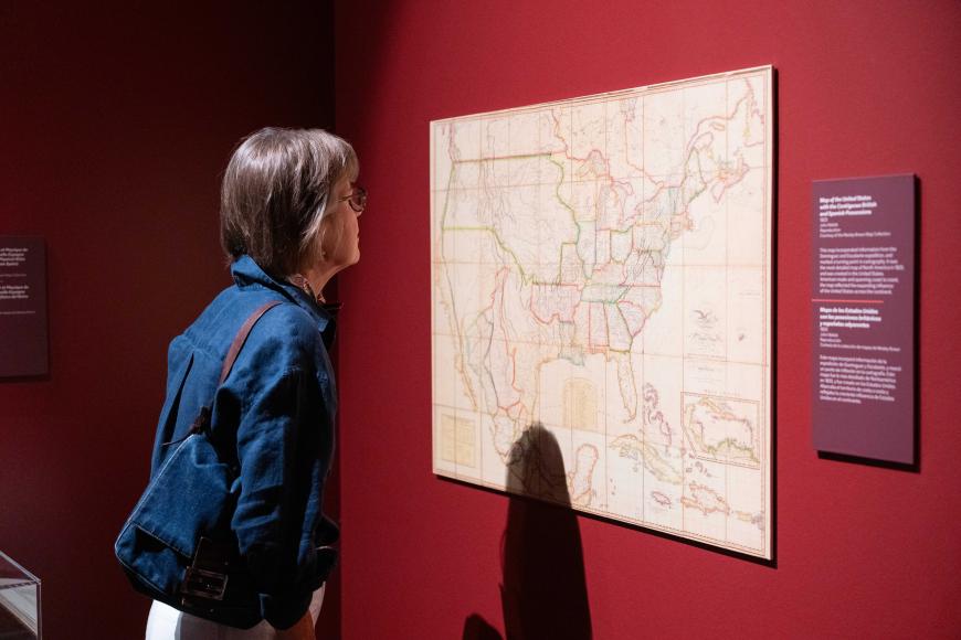 A museum guest looks closely at a large map on the wall of 1776.