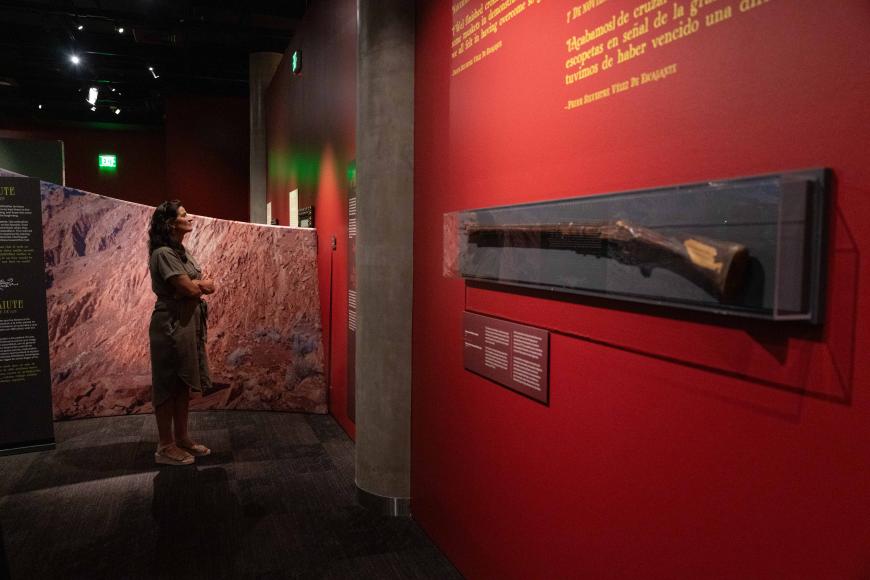 A museum guest reads a panel in the red exhibition space. In front of her is an old musket in a display case.
