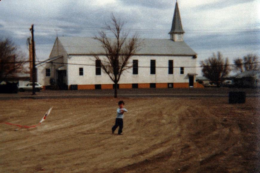 A young boy flies a kite in front of a white church.