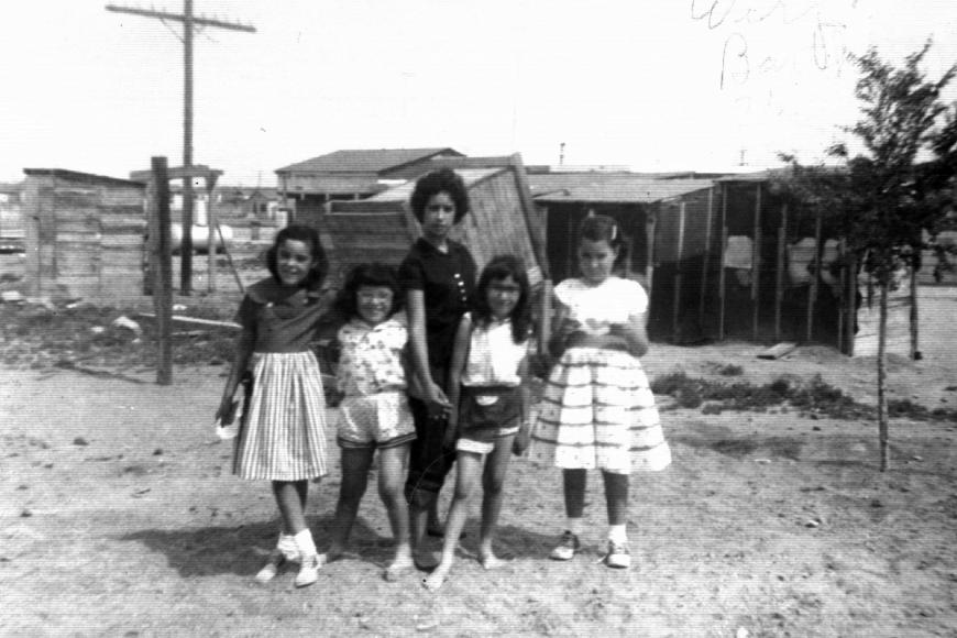 A mother and 4 young girls post in front of a small wooden structure.