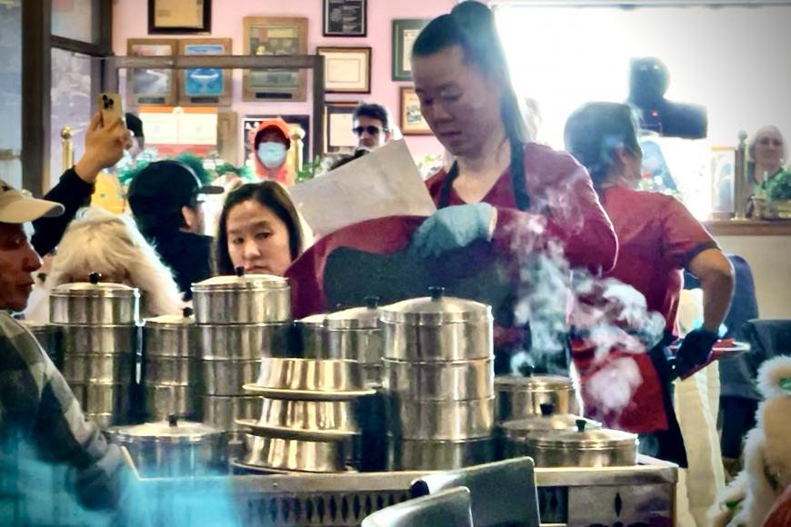 A food server carts around a large stack of dim sum containers in a busy restaurant.