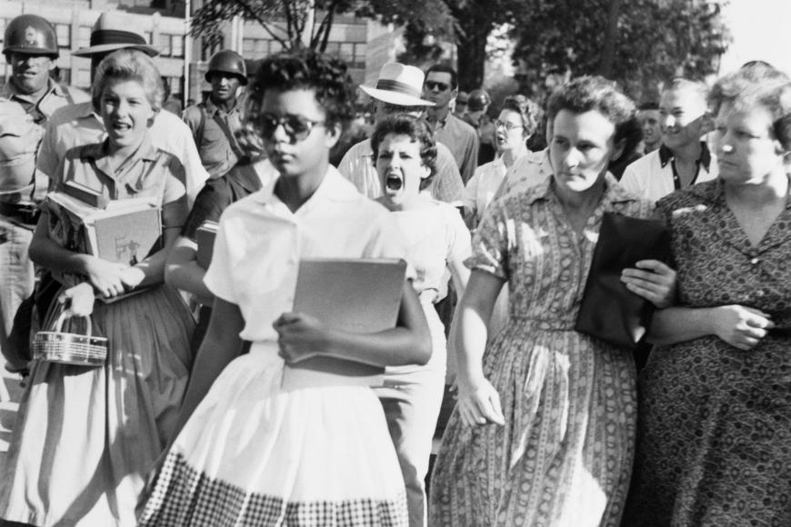 Elizabeth Eckford walks unbothered in a dress and sunglasses despite the hostile screams and stares of fellow students in the background.