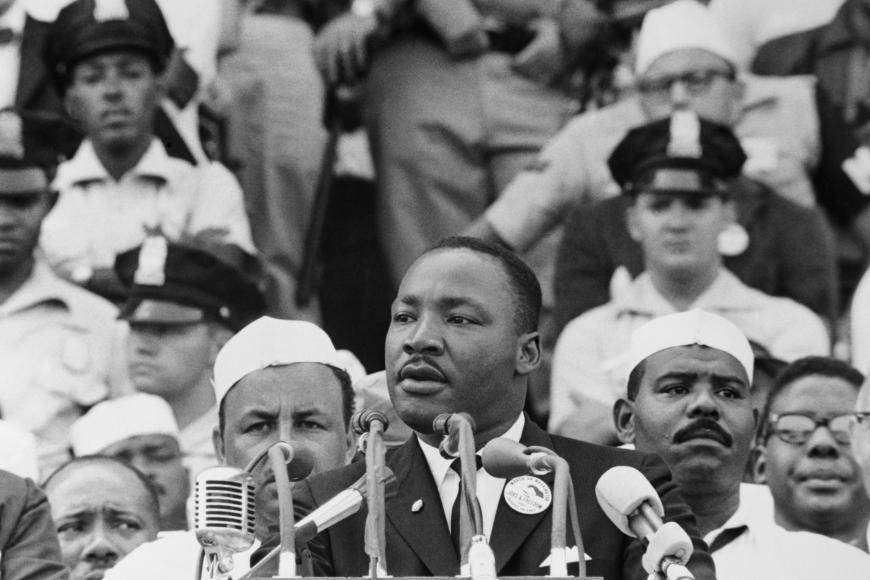  Dr Martin Luther King Jr speaks into a microphone with a crowd behind him.
