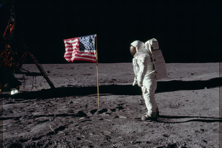 Buzz Aldrin in a space suit on the moon next to an American Flag