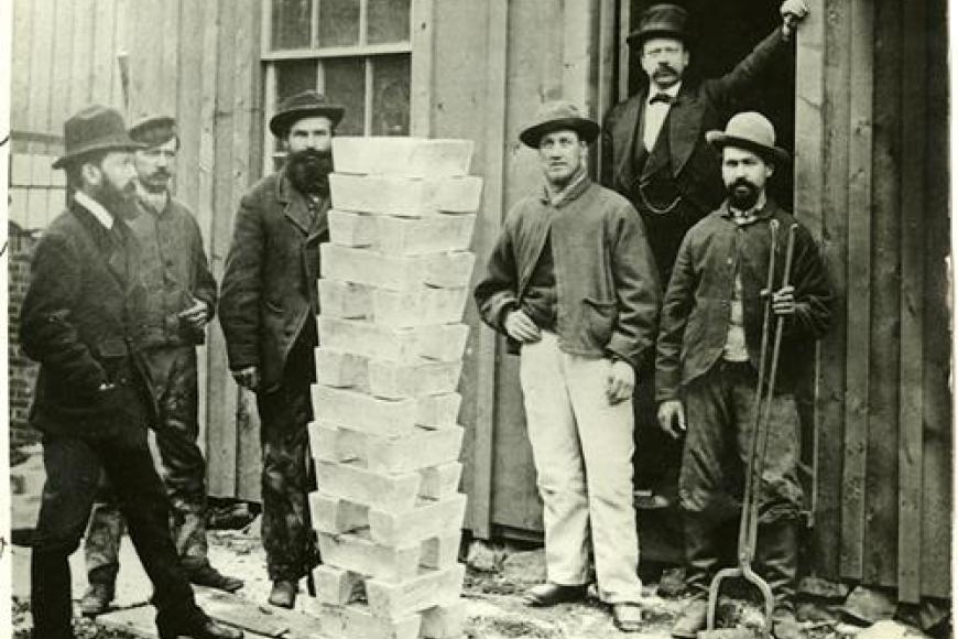 fOur men stand around a large stack of silver ingots that is nearly as tall as them.