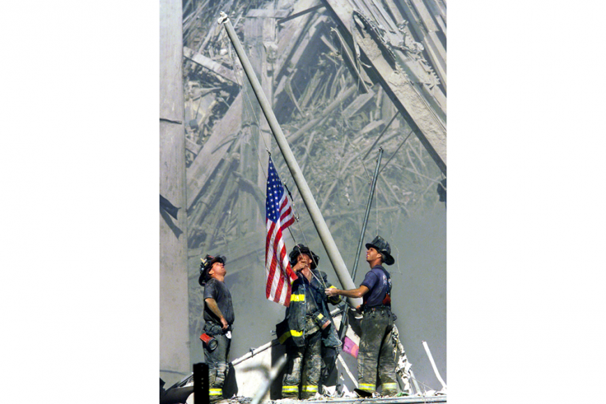 Together, three New York fireman raise an American flag near the still smoking rubble of the World Trade Center .