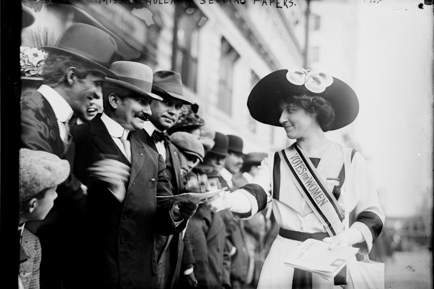 Suffragist Inez Milholland handing pamphlets to a rowdy group of men.