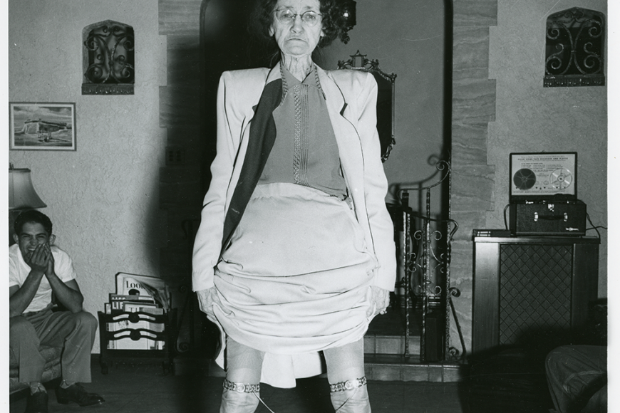 An older adult woman hikes up her dress to show her garters in a rebellious pose.