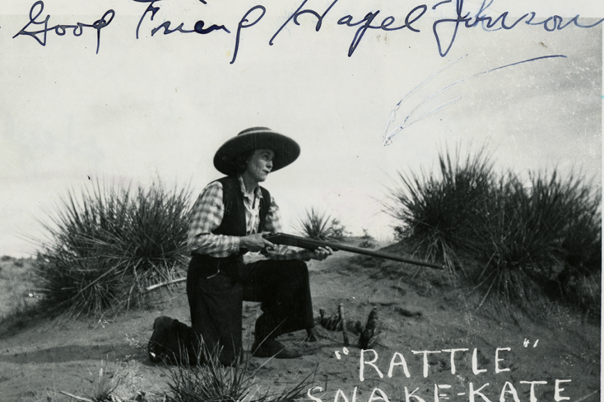 Photo of Rattlesnake Kate on one knee, holding a rifle and wearing a wide-brimmed hat.