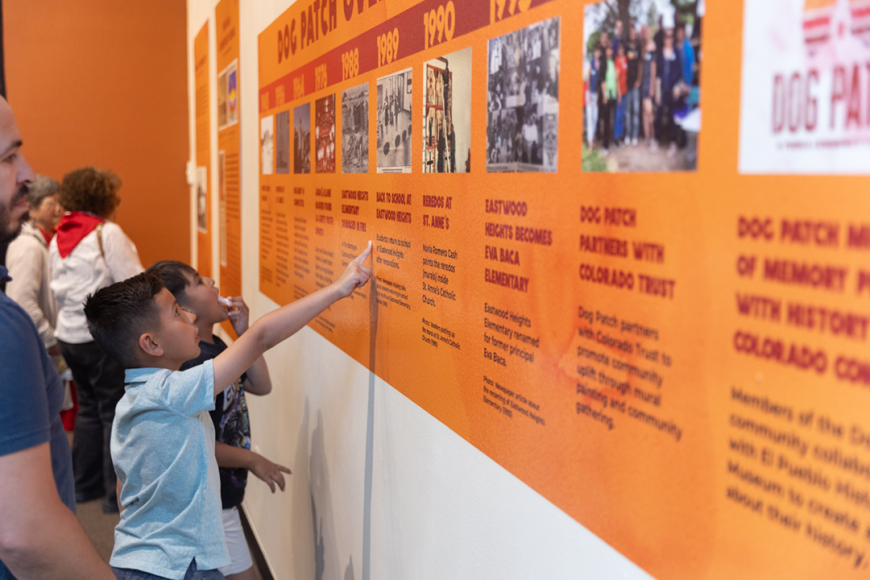 A pair of children point at a bright orange timeline of Dog Patch printed on a white wall.